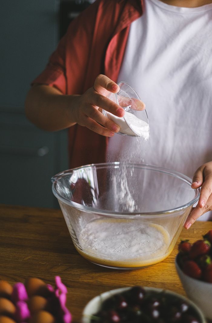 Offerings A person adding ingredients to a bowl in a kitchen, highlighting food preparation.