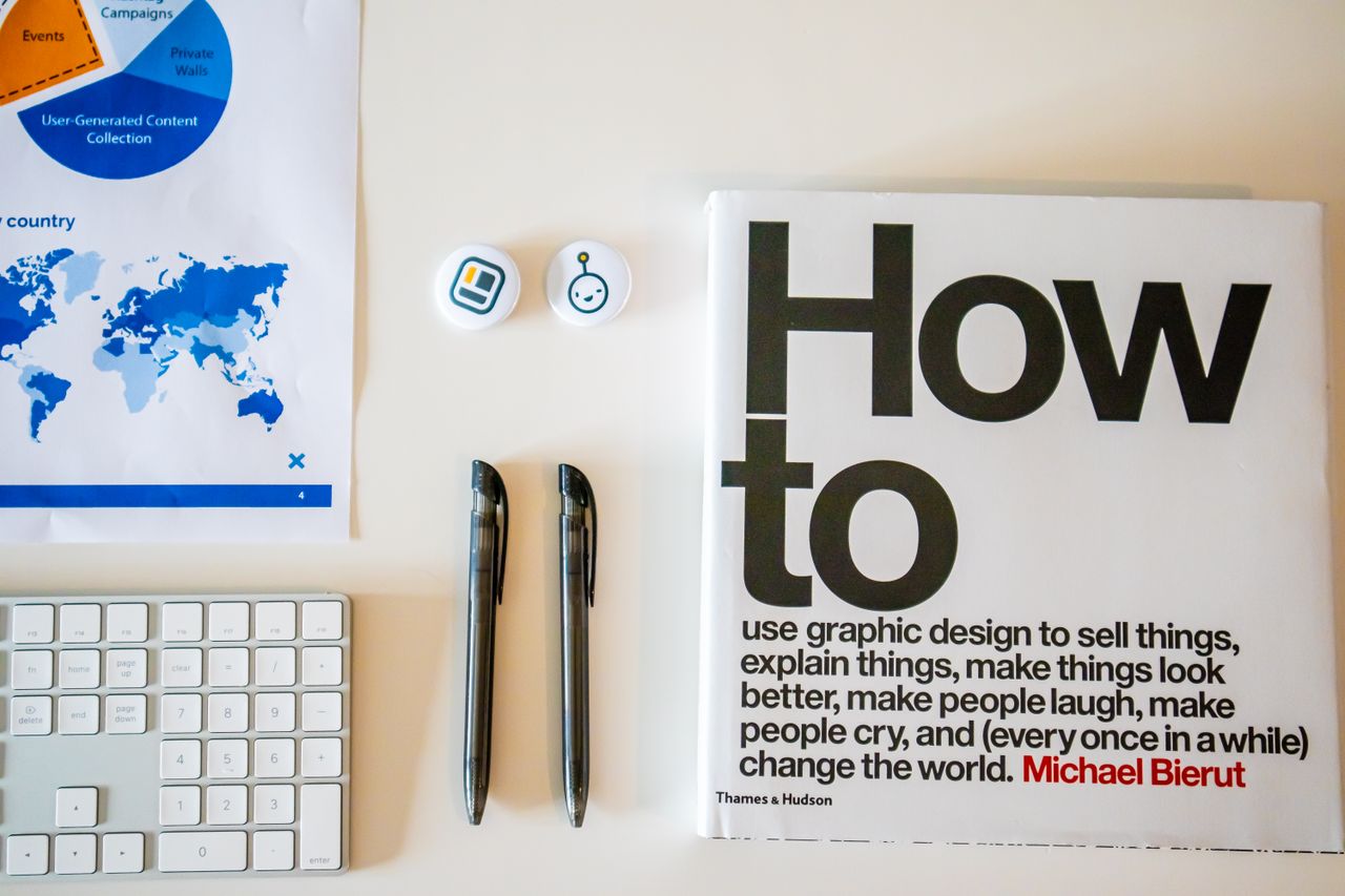 Offerings Flat lay of a creative workspace with 'How To' book, chart, pens, and keyboard in minimalist style.